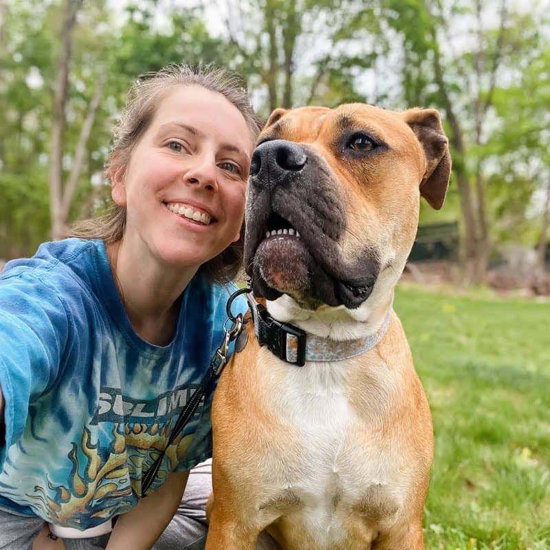 Cassidy outdoors in the grass beside a happy tan dog.